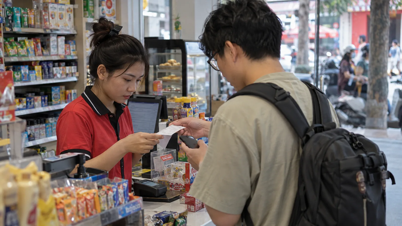 咖啡馆窗边，顾客背影手持手机查看话费余额页面，桌上放着冰咖啡